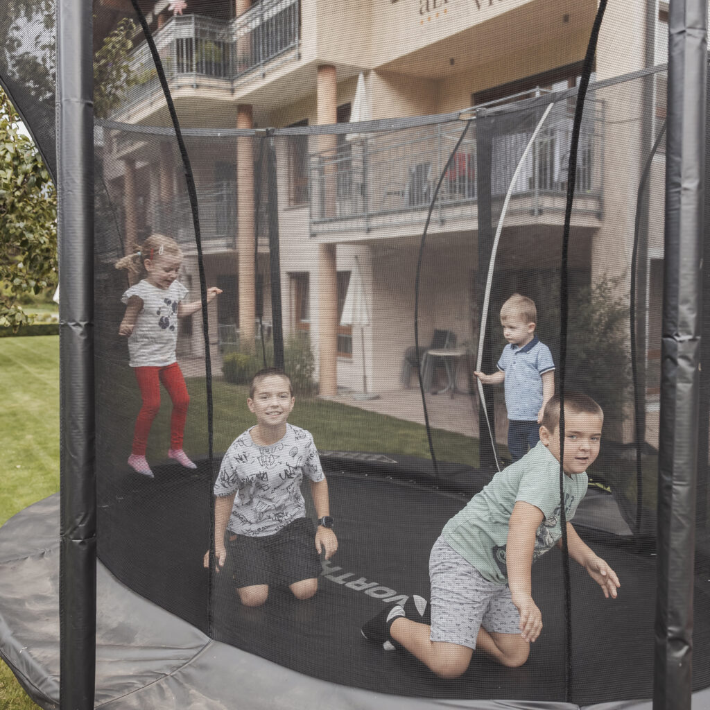 Vier Kinder spielen und springen auf einem Trampolin mit einem Sicherheitsnetz im Freien.