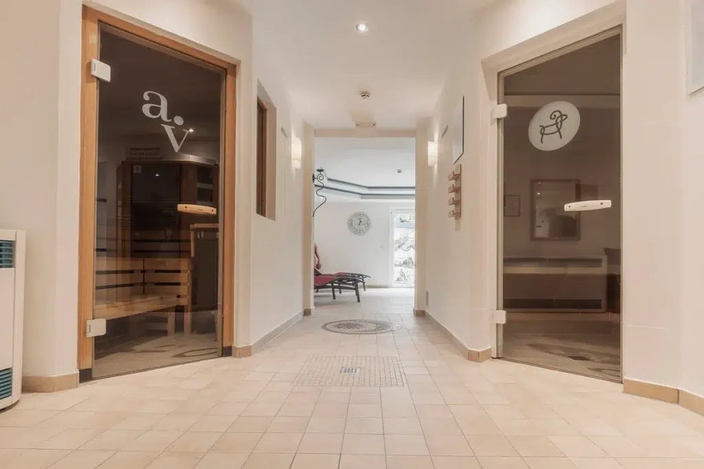 Moderner Wellnessbereich mit Glastüren, die zu den Saunen und einem Entspannungsbereich in der Mitte führen.