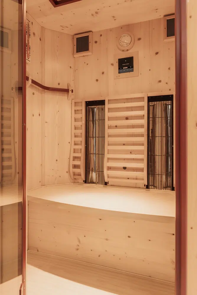 Innenraum einer Holzsauna mit Bänken, Heizplatten und einer Wanduhr.