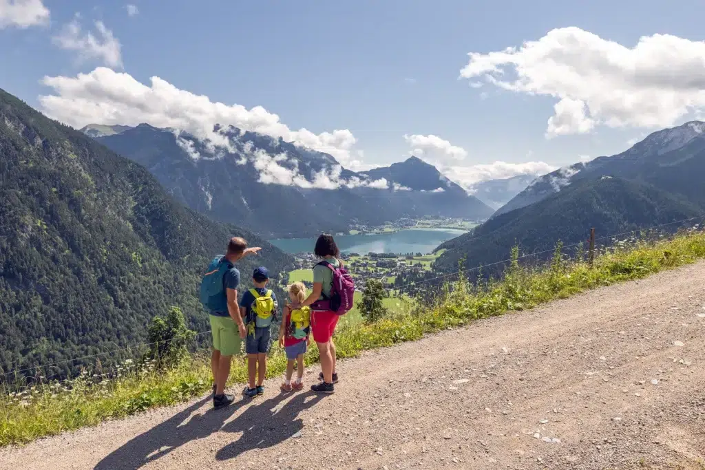 Eine Familie steht auf einem Bergpfad mit Blick auf einen See und ein von Bergen umgebenes Tal.