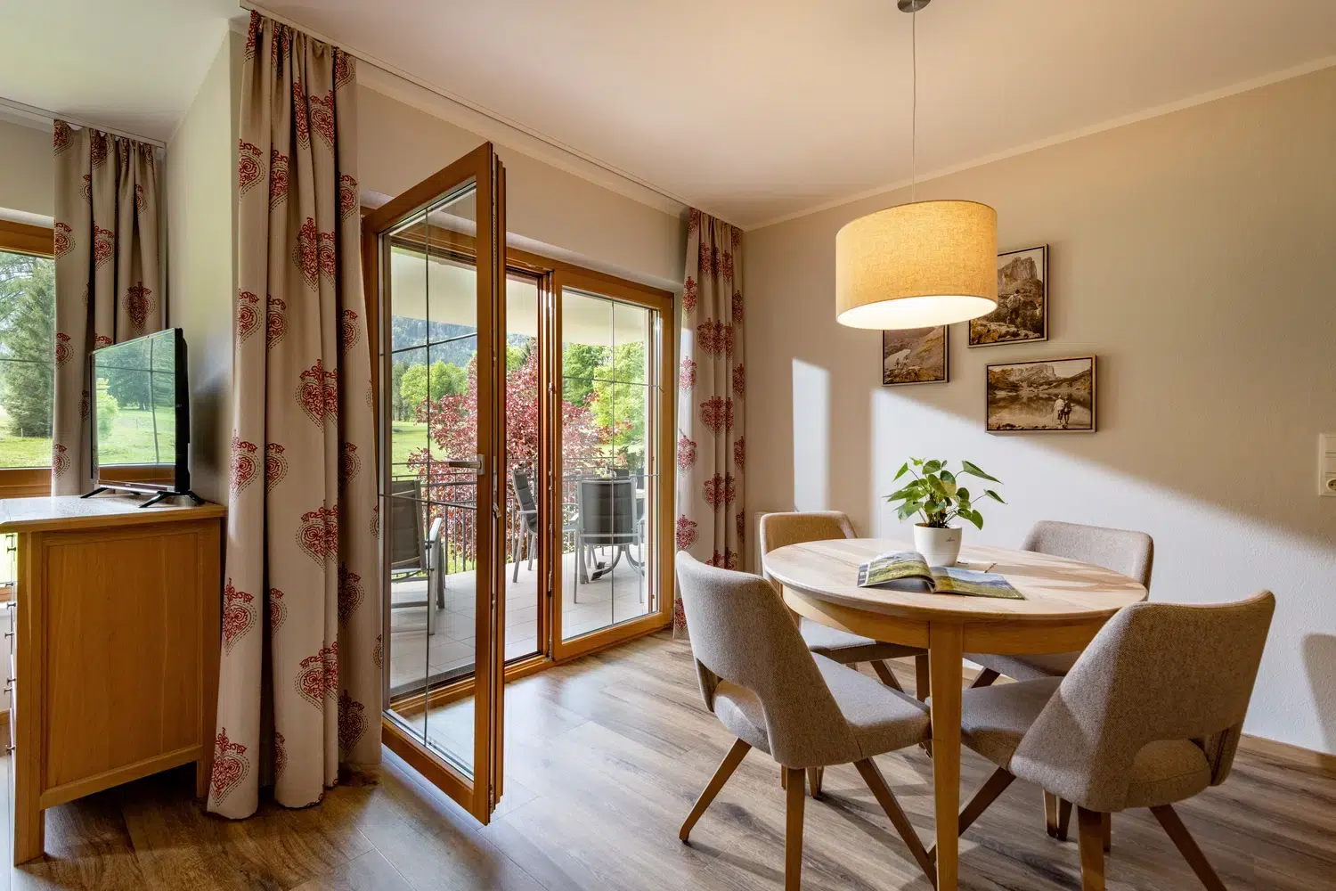 Essecke mit rundem Tisch, vier Stühlen und offener Tür zu einem sonnigen Balkon.