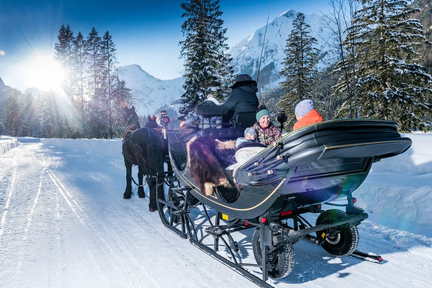 Ein Pferdeschlitten befördert Menschen durch eine verschneite, bergige Winterlandschaft.